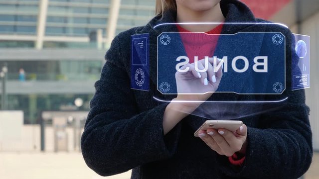 Unrecognizable woman interacts HUD hologram with text Bonus. Girl in the coat uses the technology of the future mobile screen on the background of the city