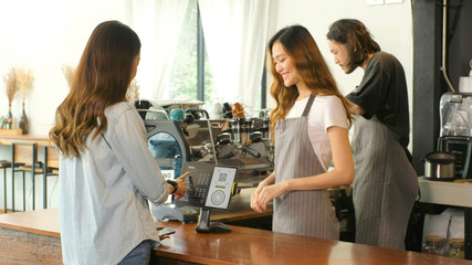 Young asian woman ordering coffee by digital tablet with barista, waitress, small business owner at counter in coffee shop cafe background, small business concept