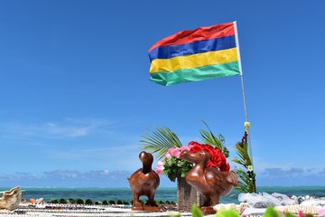 Picture of a wooden statue representing the symbol of Mauritius the Dodo bird. Mauritius flag in...