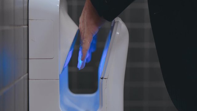 Business man in formal suit and white shirt is using hand dryer in a public toilet or lavatory