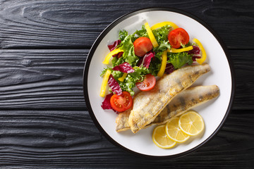 Freshwater fish fillet of zander fried with fresh vegetables and lemon close-up in a plate. Horizontal top view