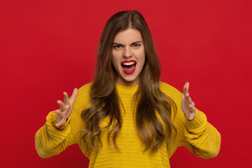 angry pretty girl in yellow sweater with red lips gesturing and screams loudly, expresses irritation, isolated on red background. Stop it please