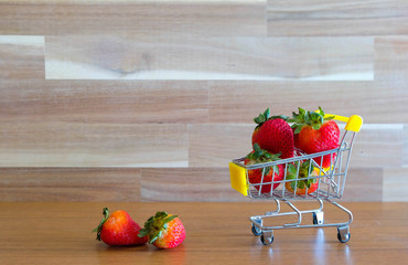 Close up strawberry on shopping cart with white and brown wooden background text advertising, diet...