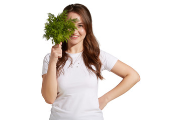 Veganism as a way of living is demonstrated by a smiling brunette girl in a white tee. The healthy looking lady is holding a fennel bunch in front of her face. 