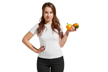 Fototapeta na wymiar Veganism as a way of living is demonstrated by a pretty brunette girl in a white tee and black jeans. The healthy looking lady is showing two yellow and green peppers in her hand. 