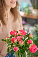 Coral peonies in a glass vase. The woman holds in her hands. Beautiful fresh cut bouquet, the work of the florist at a flower shop.