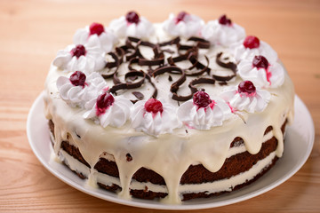 Chocolate vanilla cake with cherry jelly, topped with white cheese frosting and chocolate pieces