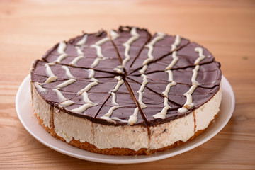 Sweet chocolate spider web cake with frosting on top served on a white plate on light wooden background.