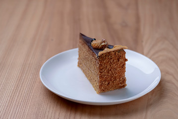 Delicious nut cake glazed with dark chocolate icing served on a white plate on light wooden table background.