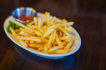Serving of french fries with tomato sauce on white plate on dark wooden background