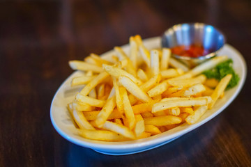 Serving of french fries with tomato sauce on white plate on dark wooden background