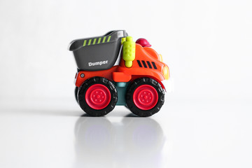 Plastic dump truck toy construction vehicle isolated on white background with reflection. Dumper side view. Orange vehicle with red wheels and name text. Operator in red hard hat