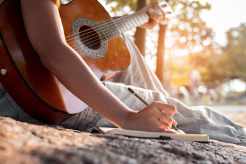 Songwriter writing on notebook with acoustic guitar.
