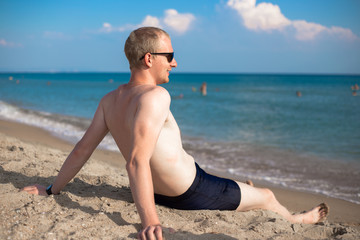 resting young man sits on the sand on the shore and looks at the sea