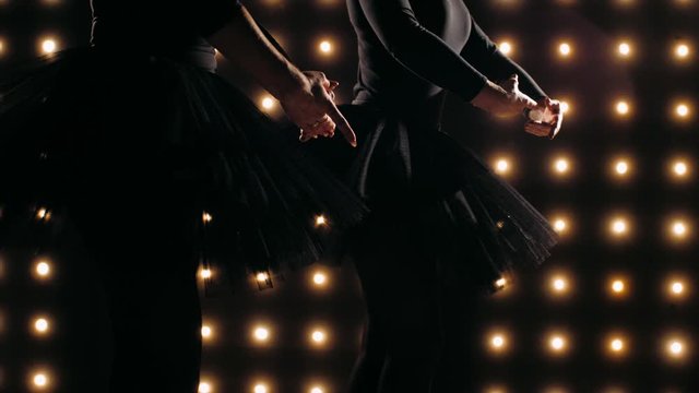 Silhouettes of two ballerinas in black tutu is dancing ballet in the dark studio with the lights on the background. Ballet dancers are performs movements synchronously