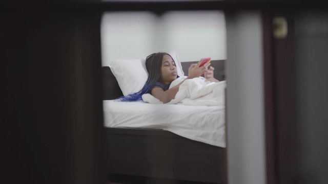 Young African American woman with dreadlocks using smartphone and smiling. Happy teenager using social media at night. Internet addiction, lifestyle.
