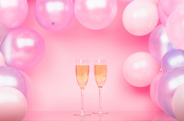 Two glasses of champagne on a pink background with pink and purple balloons. Bright background for celebration.