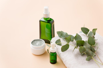 beauty, spa and wellness concept - serum, clay mask, oil and eucalyptus cinerea on bath towel