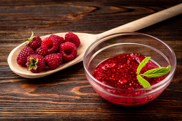 Raspberry jam on dark wooden background.