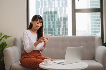 Obraz premium Young woman in casual clothes sitting on sofa at cozy home interior. Technology and communication concept.