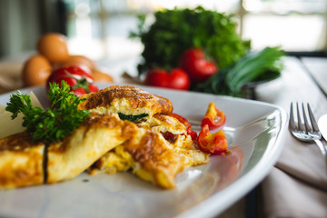 Traditional omelet with vegetables, spinach, tomatoes and herbs on a wooden table in a restaurant.