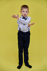 Portrait of a cute 10 years old schoolboy boy on a yellow background. Standing straight at full height, Showing emotions, talking.