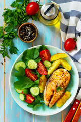 Dietary and healthy nutrition. Grilled salmon steak and baked potatoes with fresh vegetable salad on a wooden table. Top view on a flat background.