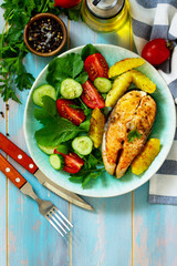 Dietary and healthy nutrition. Grilled salmon steak and baked potatoes with fresh vegetable salad on a wooden table. Top view on a flat background. Copy space.