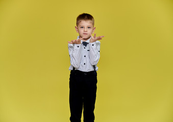 Portrait of a cute boy 10 years old schoolboy on a yellow background in trousers and a shirt. Standing right in front of the camera, Shows emotions, talks in different poses.
