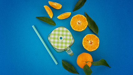 Flat lay of sliced citrus clementines with green leaves and juice jar fresh juice concept on blue background