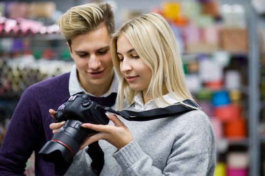 Pretty blond girl photographing a handsome blond guy in a decor shop