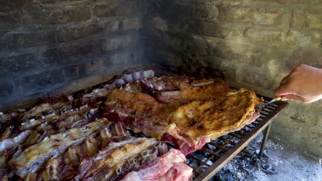 Man hands moving around pieces of beef meat in Argentinian asado to cook evenly