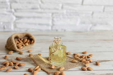 Almond oil in bottle and almond nuts on wooden background.