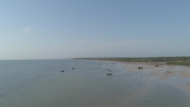 Aerial push in of beach with local African people, birds, boat dhow at low tide