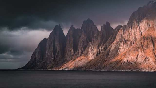 Shadows crawling over the mountain ridge. Dark gloomy clouds passing above the stormy waters of the fjord. A timelapse video shot on the Senja island.