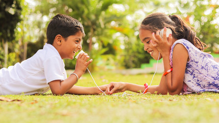 Two children having fun by playing with String Telephone at park during vacation - Concept of brain...