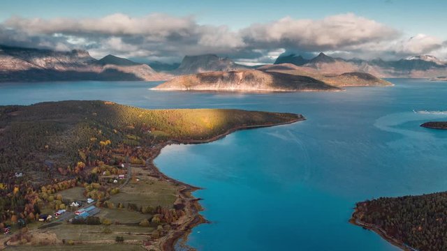 Aerial view of the beautiful northern landscape. Bright blue waters of the fjord, forest in the autumn colors, rays of sun on the ground, mountains in the background. A hyperlapse video.