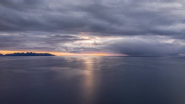 Dramatic sunset on the Andoya island. Thick stormy clouds cover the sky, narrow strip of orange sky between the sky and dark sea waters.
