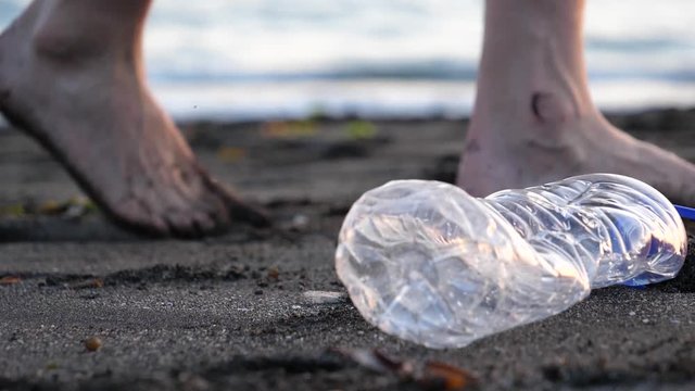 Close up of man dropping plastic bottle on beach with dead fish in the sand 