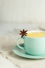 Golden Milk, turmeric latte made with curcuma, cinnamon, anise. Healthy hot winter drink, natural and organic beverage. Close up, front view. Blue mug, neutral white background, copy space for text