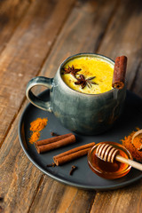 Golden milk in white mug, turmeric latte made with curcuma, cinnamon, anise, honey. Healthy hot winter drink, natural, organic beverage. Close up, front view, copy space.  Wooden rustic background