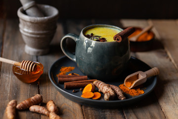 Golden milk in grey mug. Turmeric latte made with curcuma, cinnamon, anise. Healthy hot winter drink, natural, organic beverage. Close up, front view. Wooden rustic background. Raw roots as decor