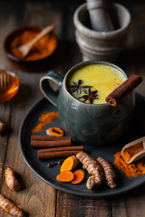 Golden milk in grey mug. Turmeric latte made with curcuma, cinnamon, anise. Healthy hot winter drink, natural, organic beverage. Close up, front view. Wooden rustic background. Raw roots as decor