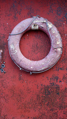 old red faded life buoy hanging on rusty with cracked paint metal door