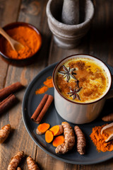olden milk in white mug, turmeric latte made with curcuma, cinnamon, anise, honey. Healthy hot winter drink, natural, organic beverage. Close up, front view.  Wooden rustic background