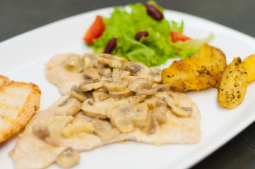 Stewed mushrooms with fish fillet, salad, fried potatoes and croutons, close-up. Tasty traditional italian food