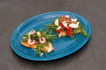 Bruschetta with shrimp, arugula, tomatoes, cheese and sauce, closeup, on gray background, high Italian cuisine