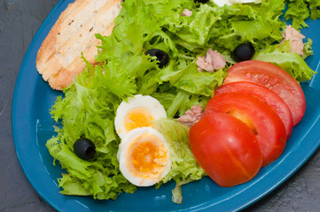 Salad with tuna, boiled eggs, tomato olives and croutons on blue plate