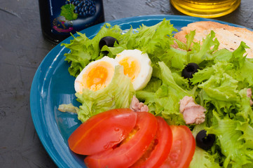 Salad with tuna, eggs, tomato, olives, spices and croutons, sauce or oil on blue plate, close-up.