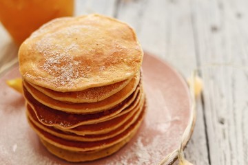 Fototapeta na wymiar Pancakes with icing sugar and orange. Pancakes in a beautiful pink plate on a light wooden background. Delicious sweet food. Holiday pancakes and Christmas garland on the background.